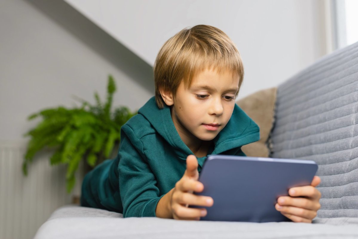 Jongen ligt op de bank en kijkt op een tablet